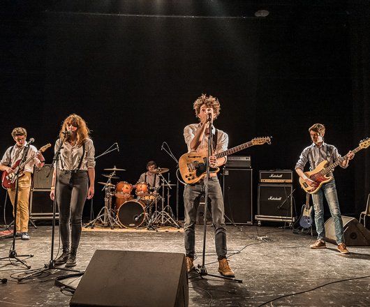 jeunes sur scène, un chanteur avec une guitare au premier plan et des musiciens derrière lui